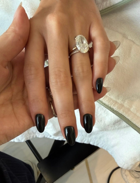 Hailey Bieber's hand is shown. She has black nails and wears a diamond ring.